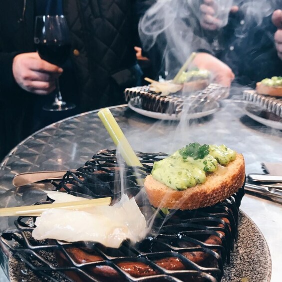 A grill with food, a glass of red wine, and a person holding a drink. 4