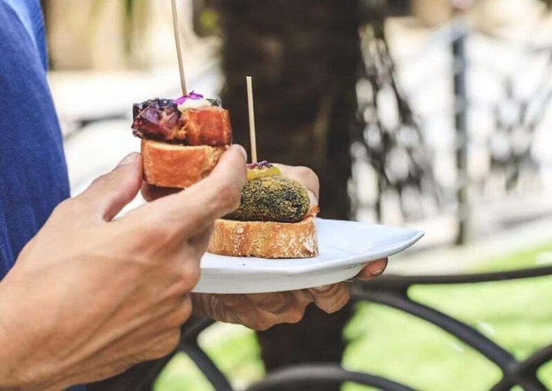 A person holding a plate with two food items, one with a toothpick. 3