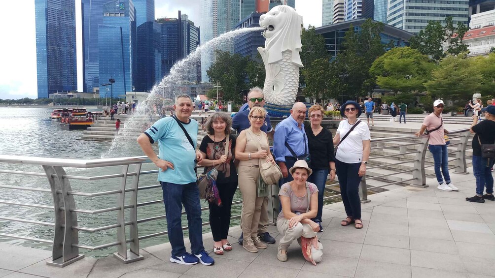 A group of people posing near a water fountain with a lion statue, with a city skyline in the background. 4