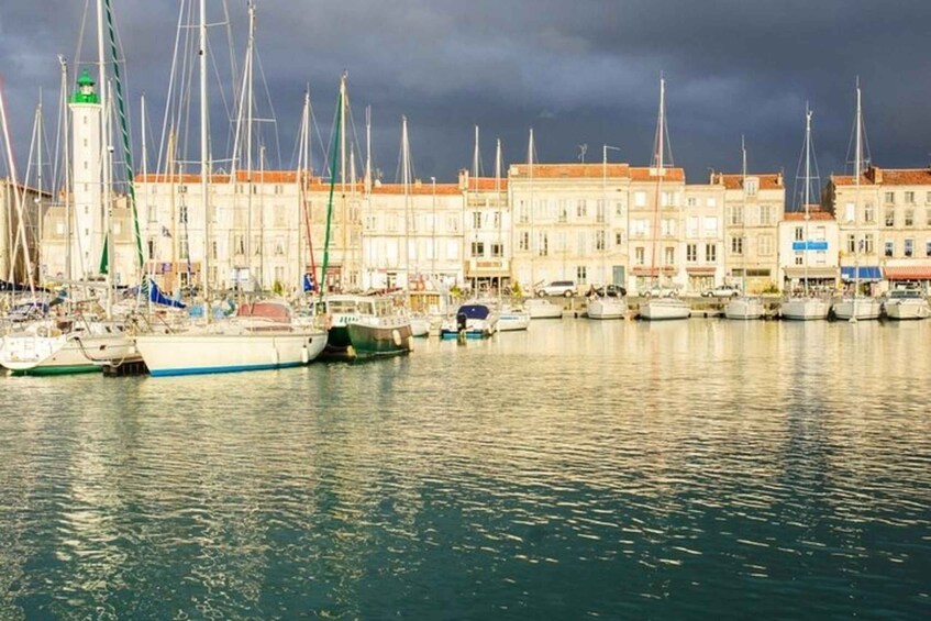 A marina with multiple sailboats docked, buildings along the waterfront, and a cloudy sky. 5