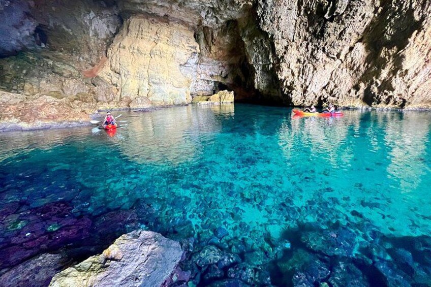 Kayakers in a clear blue cave pool surrounded by rocky walls. 3