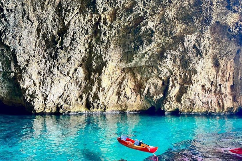 A kayaker in a red kayak on clear blue water with a rocky cliff in the background. 5