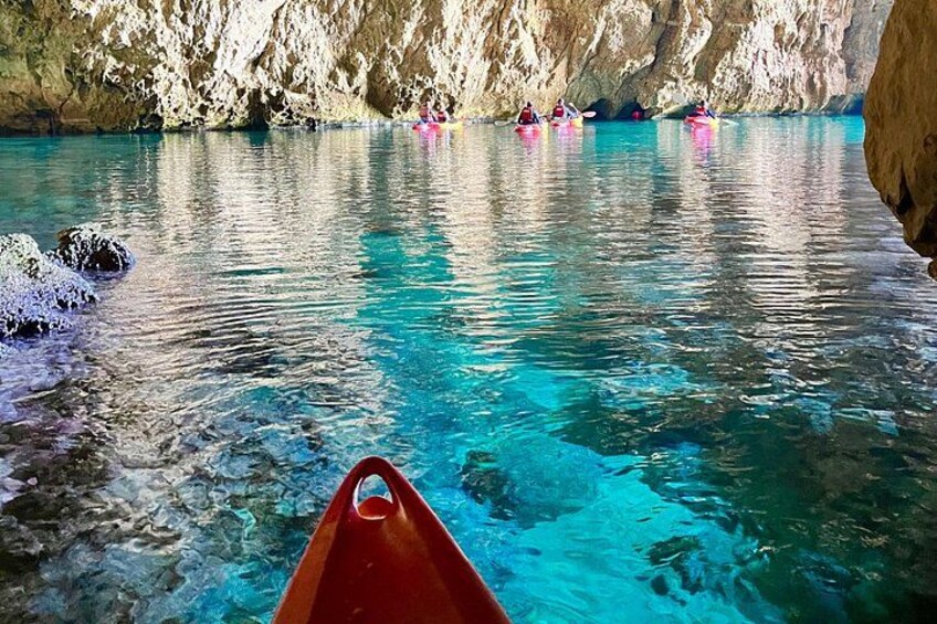 A clear blue water body with kayaks, a rocky cliff, and a red canoe. 4