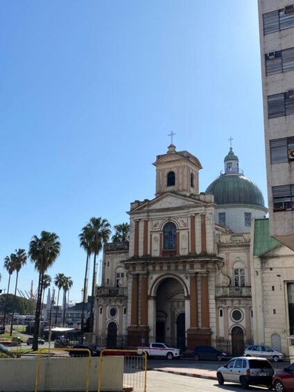 A historic church with a bell tower and dome, surrounded by palm trees and modern buildings. 5