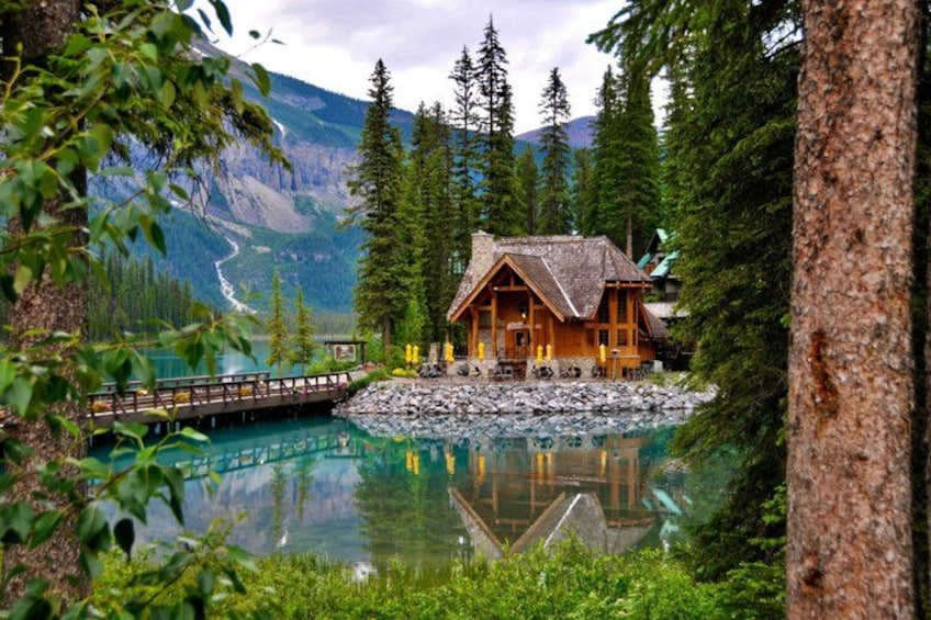 A wooden cabin by a lake surrounded by trees and mountains. 4