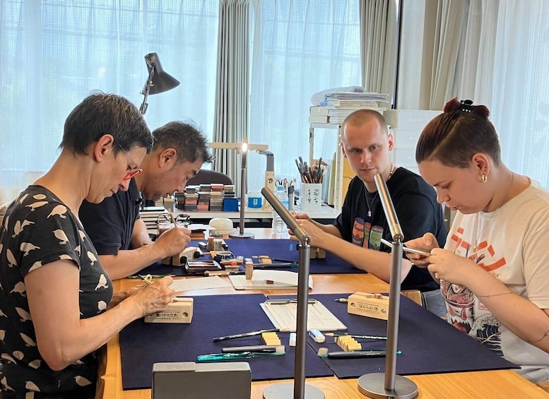 Four people sitting at a table with various stationery items and a laptop. 3