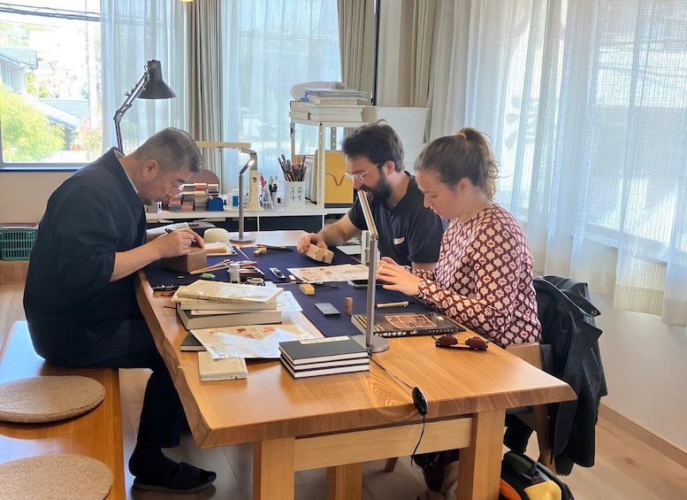 Three people working at a wooden table with books, papers, and a laptop. 5