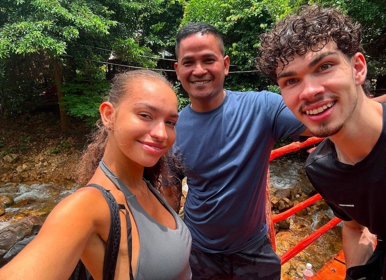 Three people standing near a river with a bridge in the background. 1