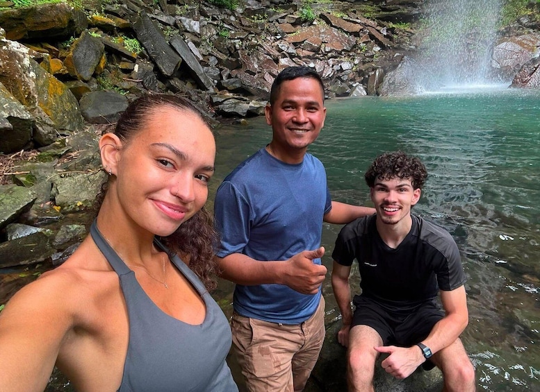 Three people near a waterfall in a rocky area with clear water. 3