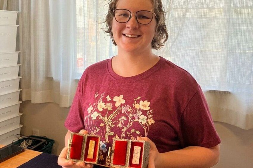 A person holding a red box with a gold design, standing in a room with a window and curtains. 4