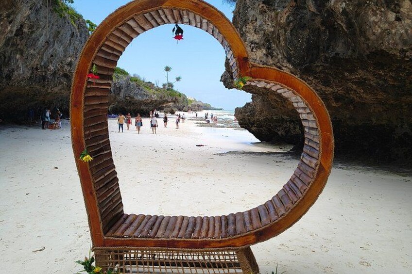 A heart-shaped wooden structure on a beach with people in the background. 5