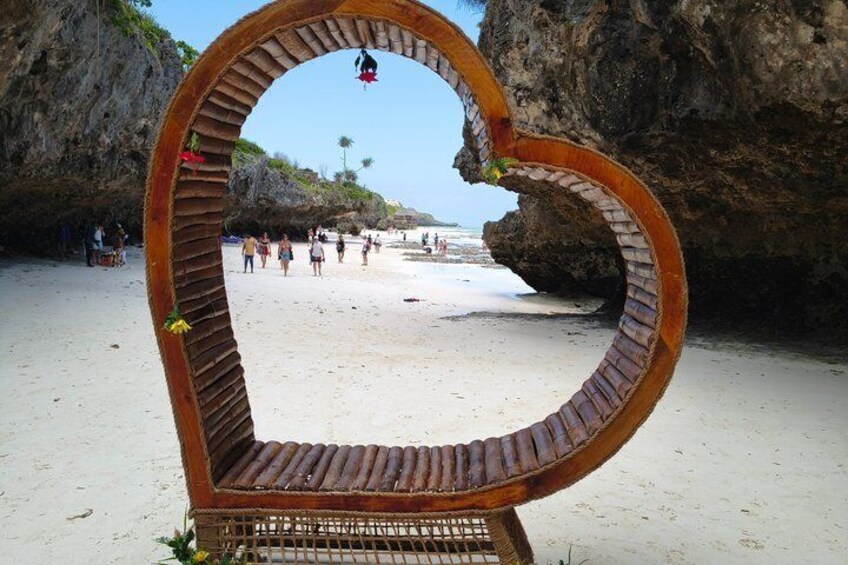 A heart-shaped wooden structure on a beach with people in the background. 5