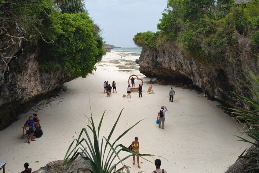 A beach with people walking and sitting, surrounded by cliffs and vegetation. 4