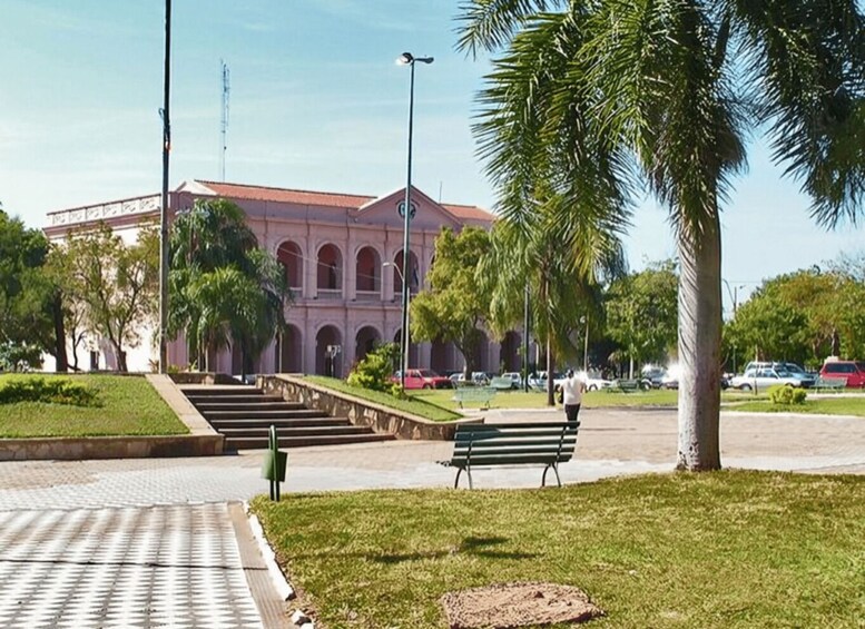 A building with arched windows and a red roof, surrounded by palm trees and a paved area with a bench. 4