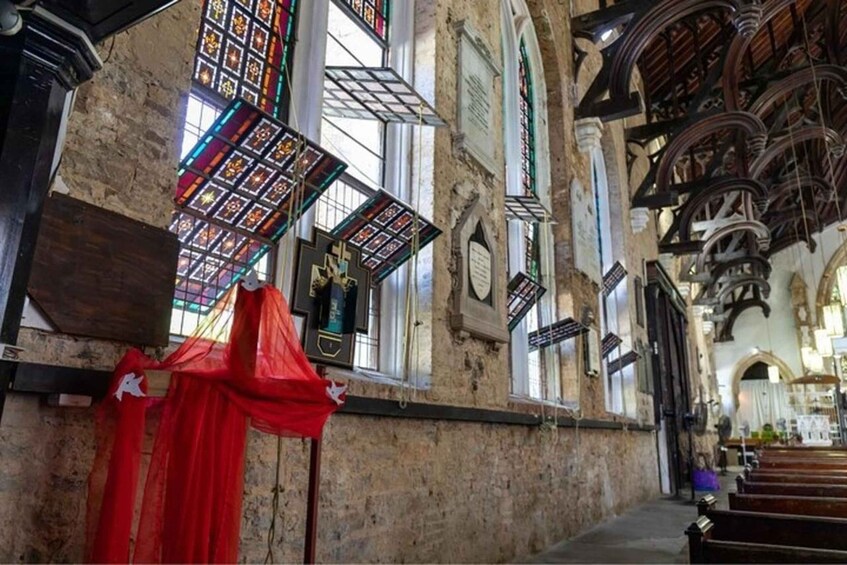A church interior with stained glass windows, wooden pews, and a red cloth draped over a column. 2
