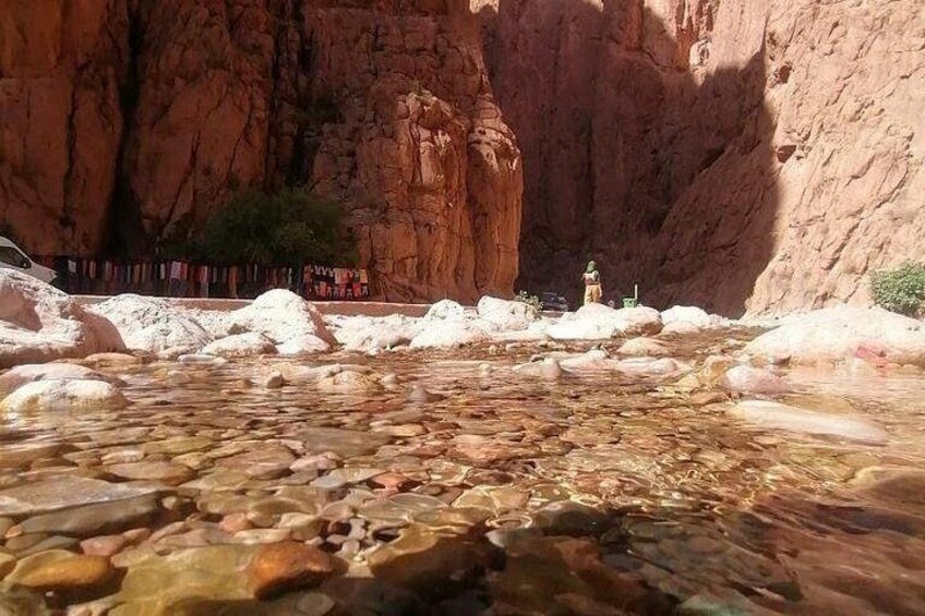 A clear stream with rocks, a small shrine, and a red rock cliff. 3