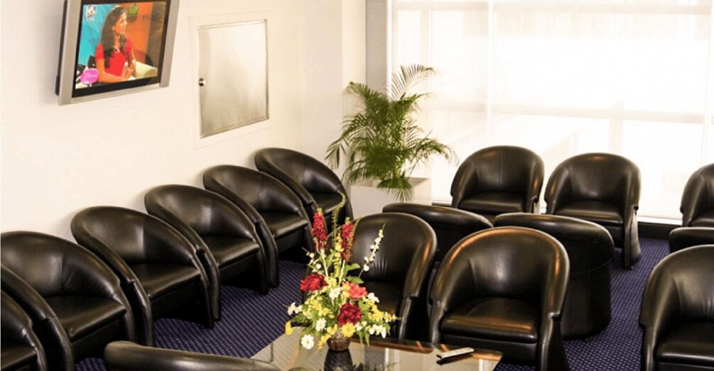 A conference room with black leather chairs, a potted plant, and a television screen on the wall. 2