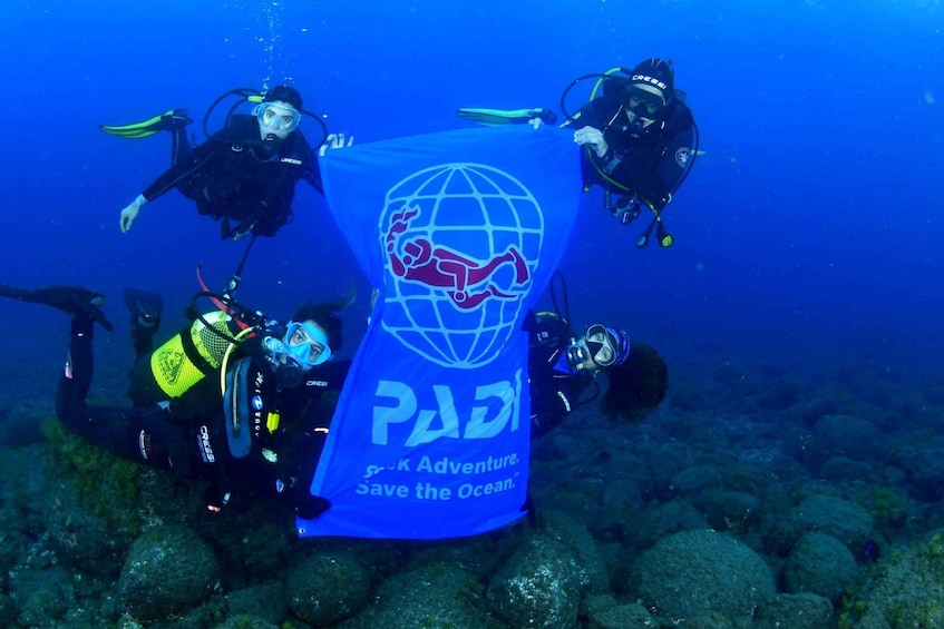 Four scuba divers underwater with a banner that reads 'PADI - P-K Adventure - Save the Ocean.' 2