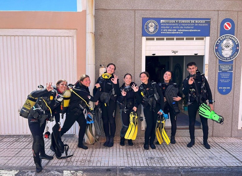 A group of divers posing in front of a building with a sign for 'LA ESCAFANDRA SERVICES DE BUCEO'. 1
