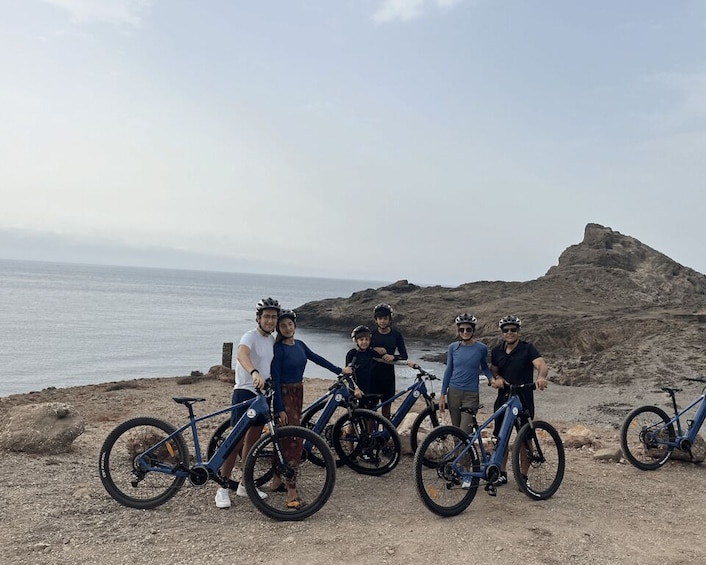 A group of people with bicycles on a rocky beach with the ocean in the background. 2