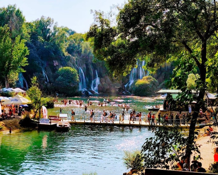 A riverside area with waterfalls, a dock, and people enjoying the water. 2