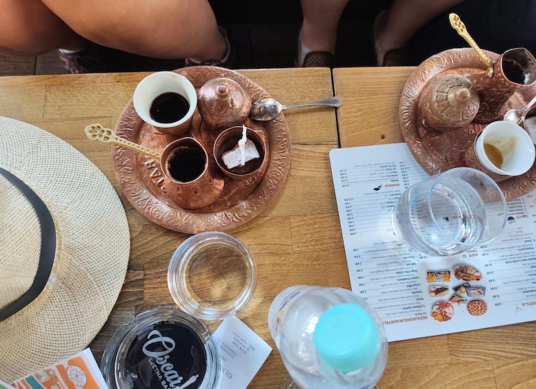 A copper tea set with cups and a teapot, a menu, a straw hat, and a bottle of water on a wooden table. 4