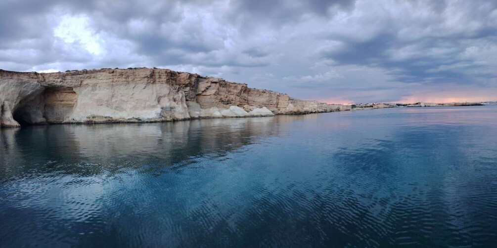 A coastal cliff with a cave entrance, calm sea, and a cloudy sky. 4