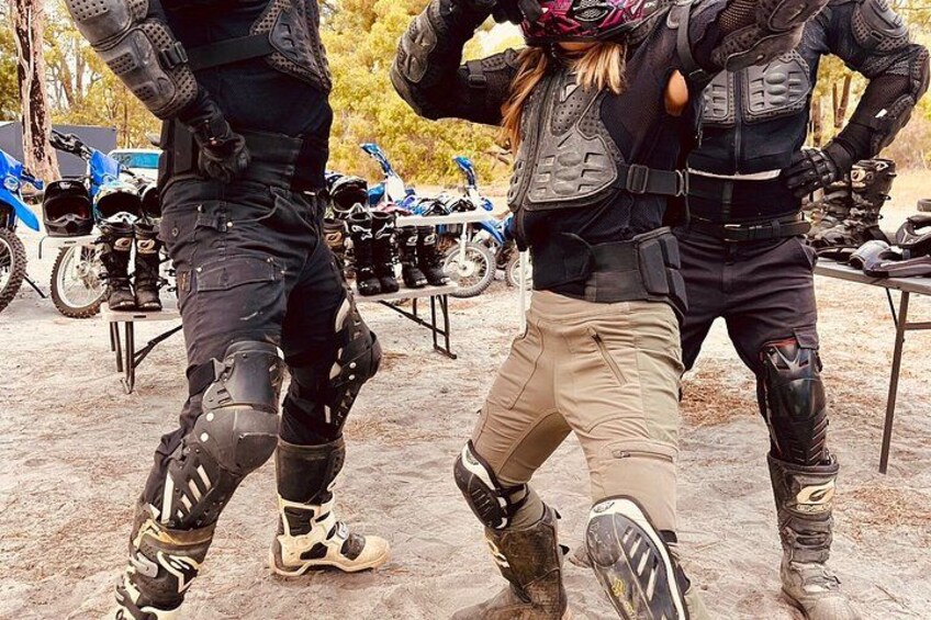 Two people in tactical gear, one with a helmet, standing in a dirt area with motorcycles in the background. 2