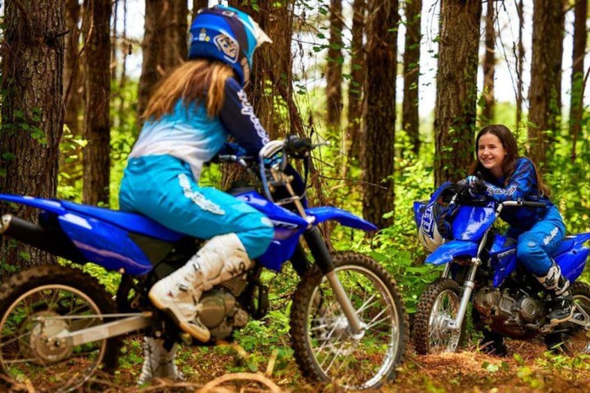 Two people on blue dirt bikes in a forest. 5