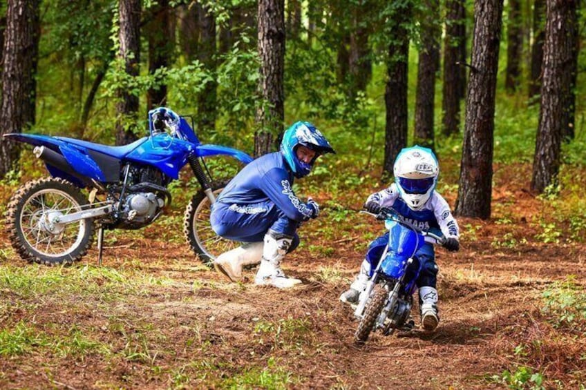 Two riders on blue dirt bikes in a forested area. 1