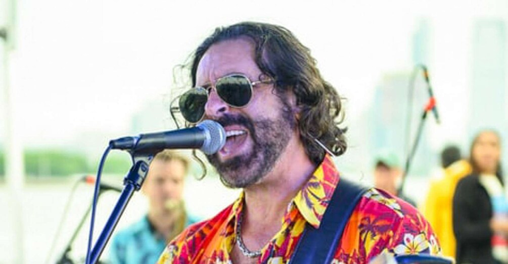 A person with long hair, wearing a colorful shirt, singing into a microphone. 4