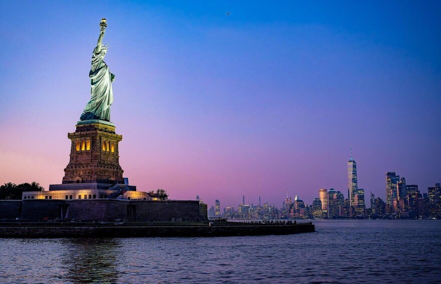 The Statue of Liberty at dusk with the New York City skyline in the background. 3