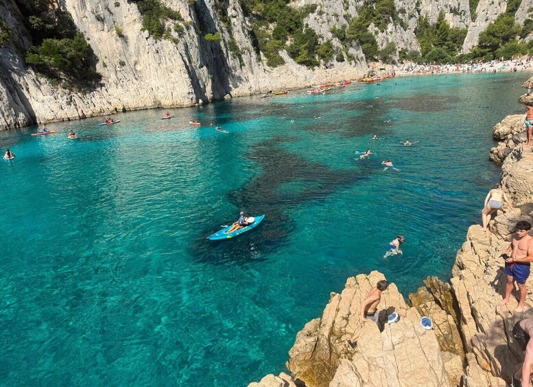 A coastal area with clear turquoise water, rocky cliffs, and people engaging in water activities like kayaking and swimming. 5