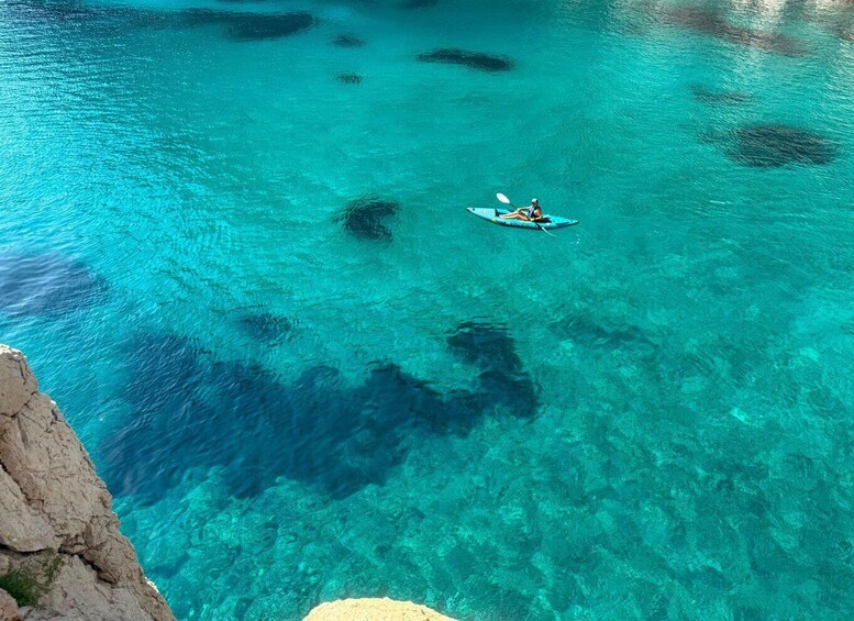 A kayaker on a turquoise sea with clear water and rocky coastline. 3