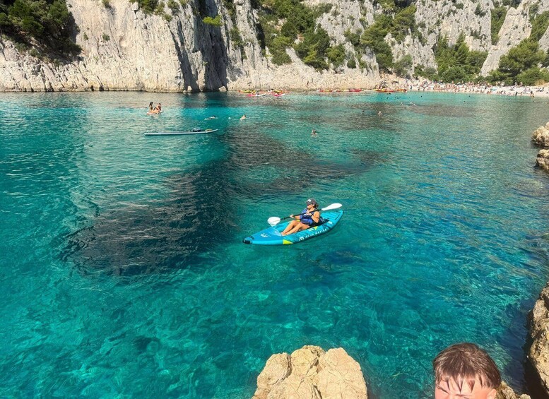 A kayaker on a turquoise sea with rocky cliffs in the background. 2