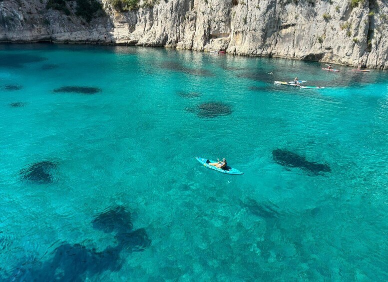 A person kayaking on clear turquoise water with rocky cliffs in the background. 1