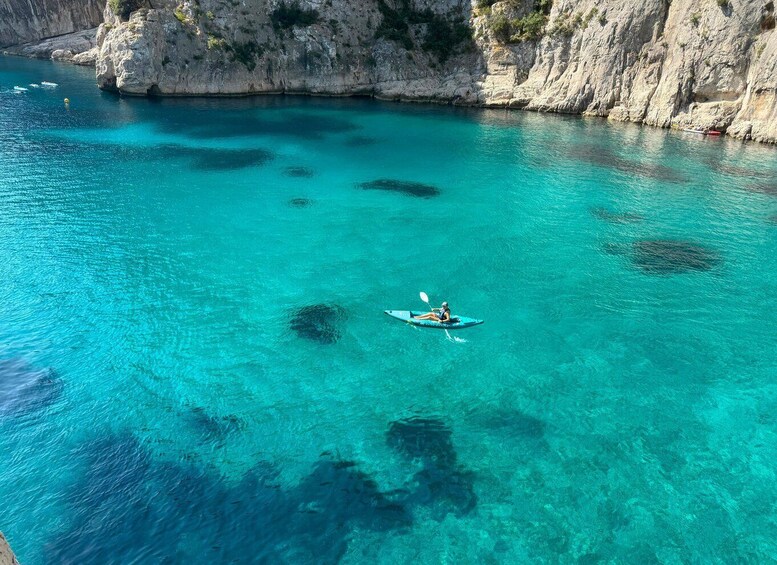 A kayaker in a turquoise sea with rocky cliffs. 4