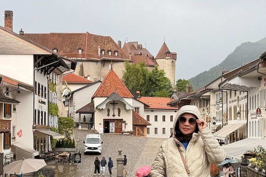 A cobblestone street with historic buildings, a castle in the background, and a person in winter clothing. 1
