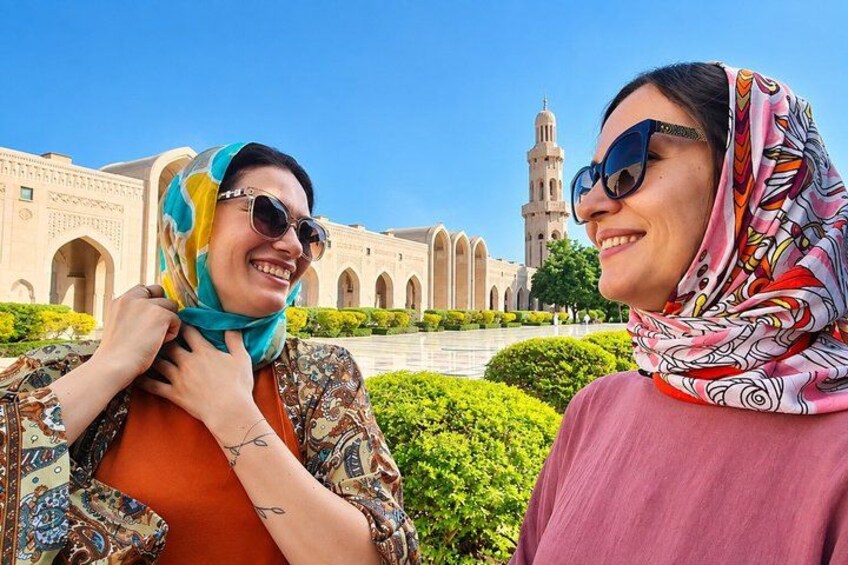 Two people in front of a historic building with arches and a minaret. 1