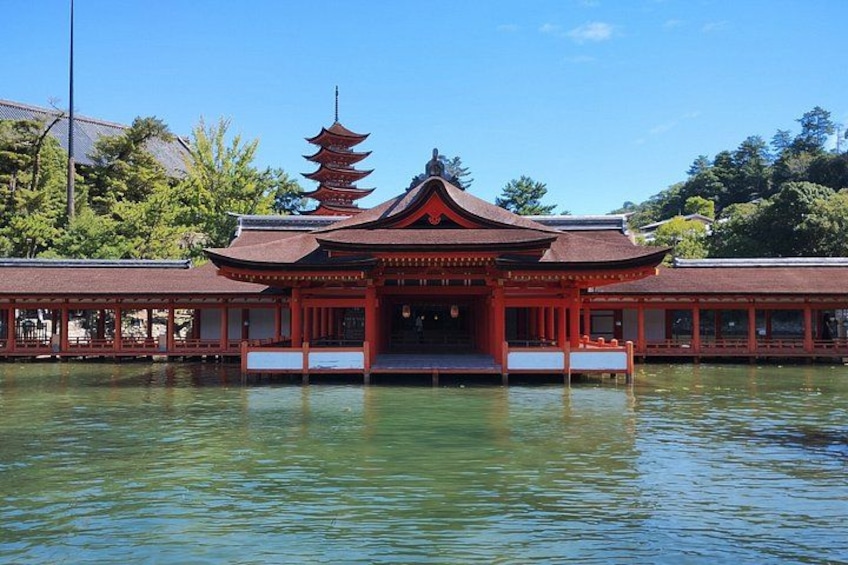 A traditional Japanese pagoda with a multi-tiered roof, a water body in the foreground, and a red building with a tiled roof. 1