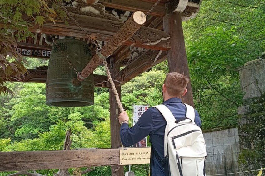 A person ringing a large bell under a wooden structure with Japanese characters. 2