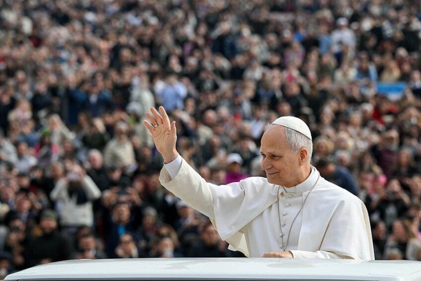 A person in white religious attire standing on a platform with a crowd in the background. 5