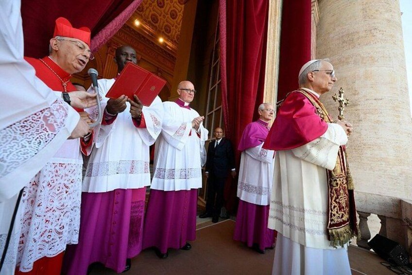 A group of clergy in ceremonial attire, holding books and a crucifix, standing in front of a building with a red curtain. 4