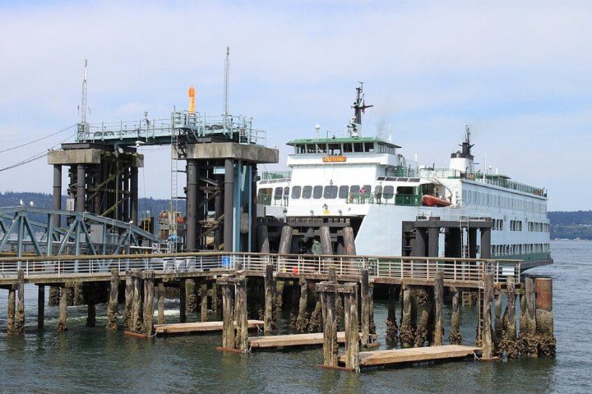 Un ferry atracado en un muelle con una embarcación blanca grande, un puente y estructuras industriales. 1