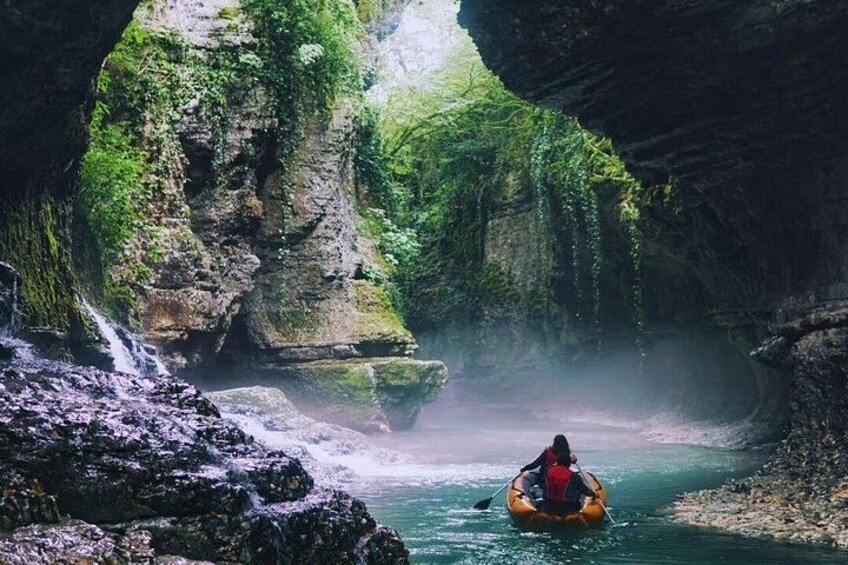 A person kayaking through a narrow canyon with lush greenery and a waterfall. 4