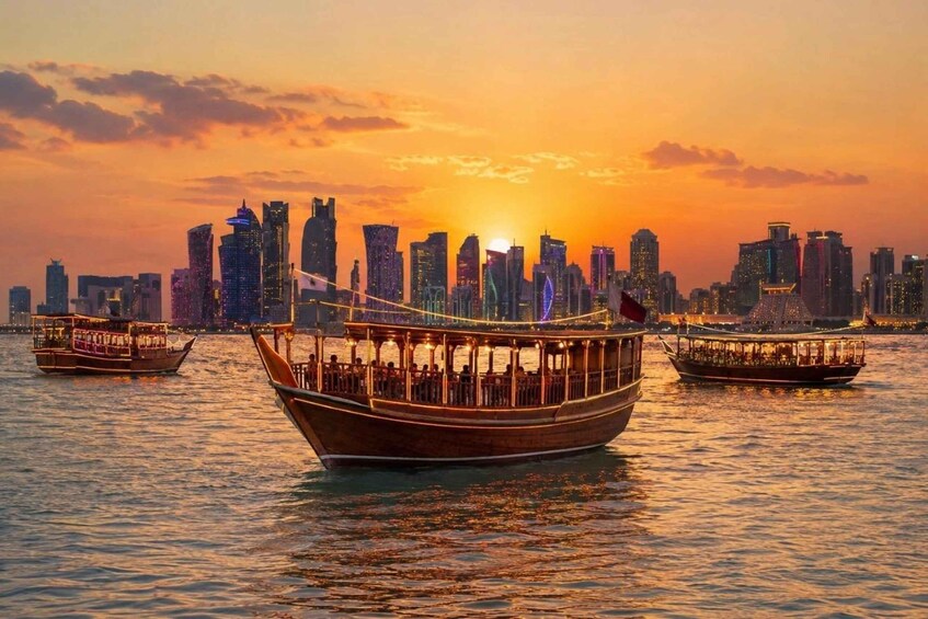 A sunset over a city skyline with modern buildings and three traditional boats on the water. 1