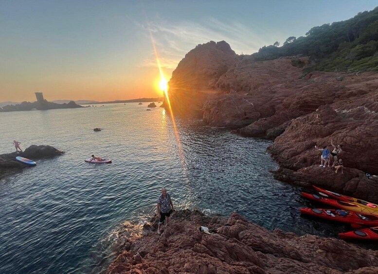 A sunset over a rocky coastline with kayaks and people near the water. 2