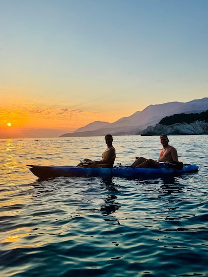 Two people kayaking on a calm body of water during sunset with mountains in the background. 4