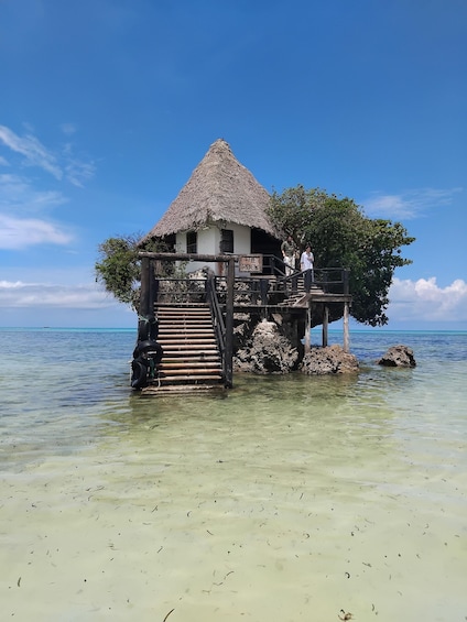 A thatched-roof structure on stilts over clear turquoise water. 1