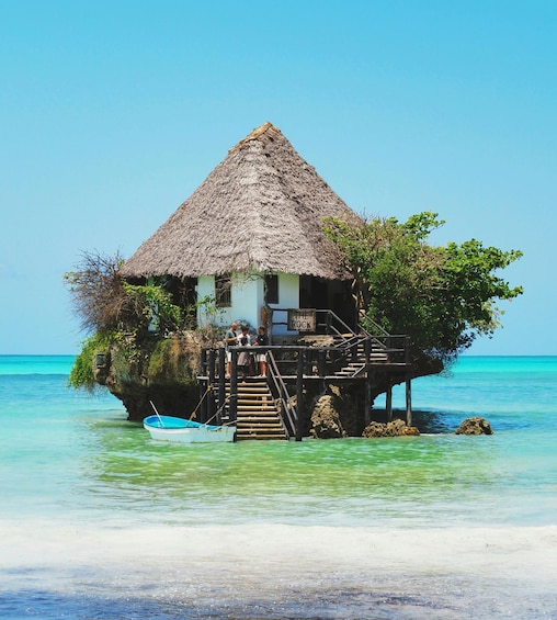 A thatched-roof house on stilts over turquoise water. 5